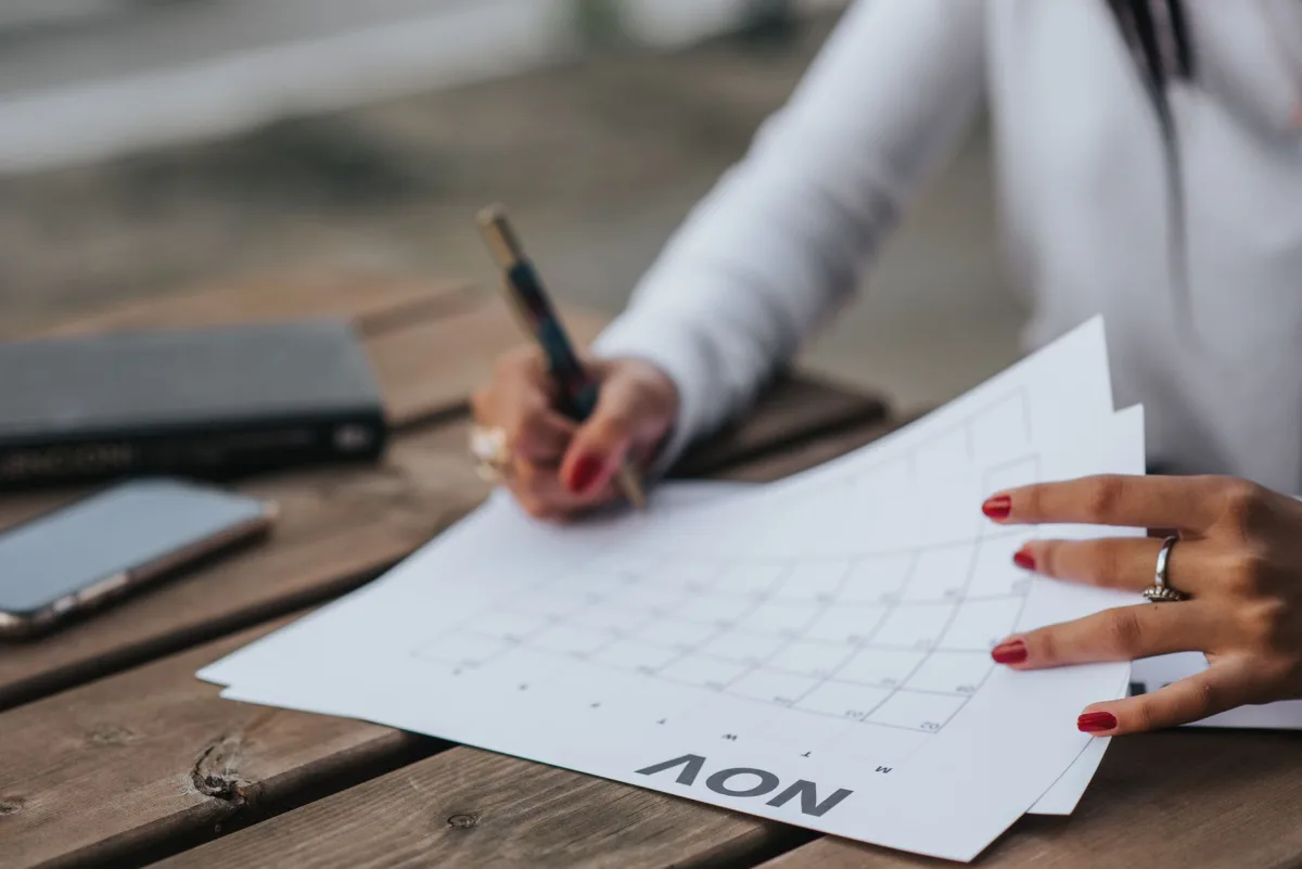 Crop faceless female in white blouse making plans month while sitting at wooden table in park Crop faceless female in white blouse making plans month while sitting at wooden table in park