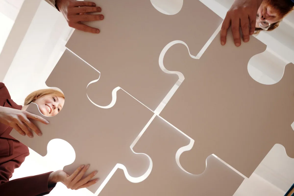 Low angle view of diverse team assembling large puzzle pieces, symbolizing unity and cooperation. Low angle view of diverse team assembling large puzzle pieces, symbolizing unity and cooperation.