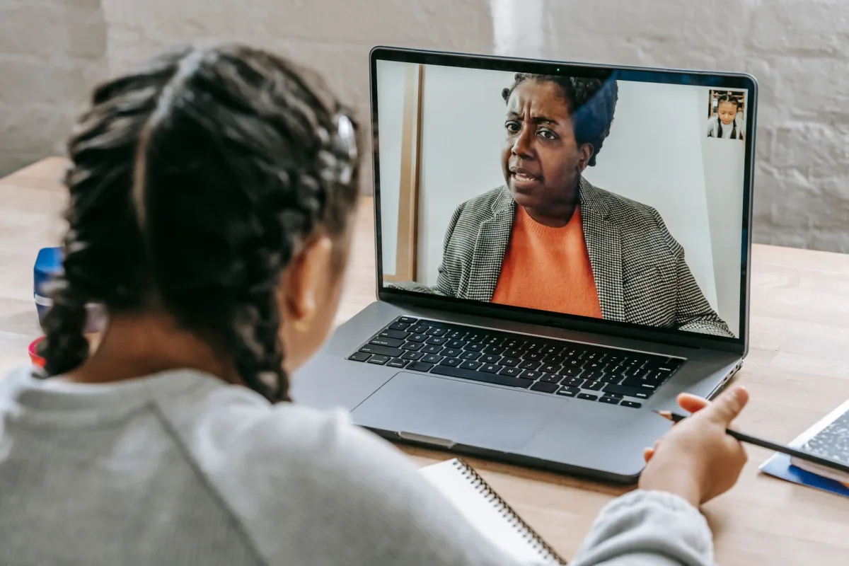 Back view of smart ethnic girl talking with tutor about test online on laptop Back view of smart ethnic girl talking with tutor about test online on laptop