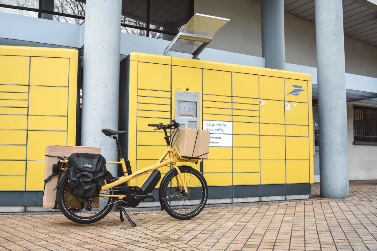 A yellow cargo e-bike loaded with parcels parked outside a package pickup station in France. A yellow cargo e-bike loaded with parcels parked outside a package pickup station in France.