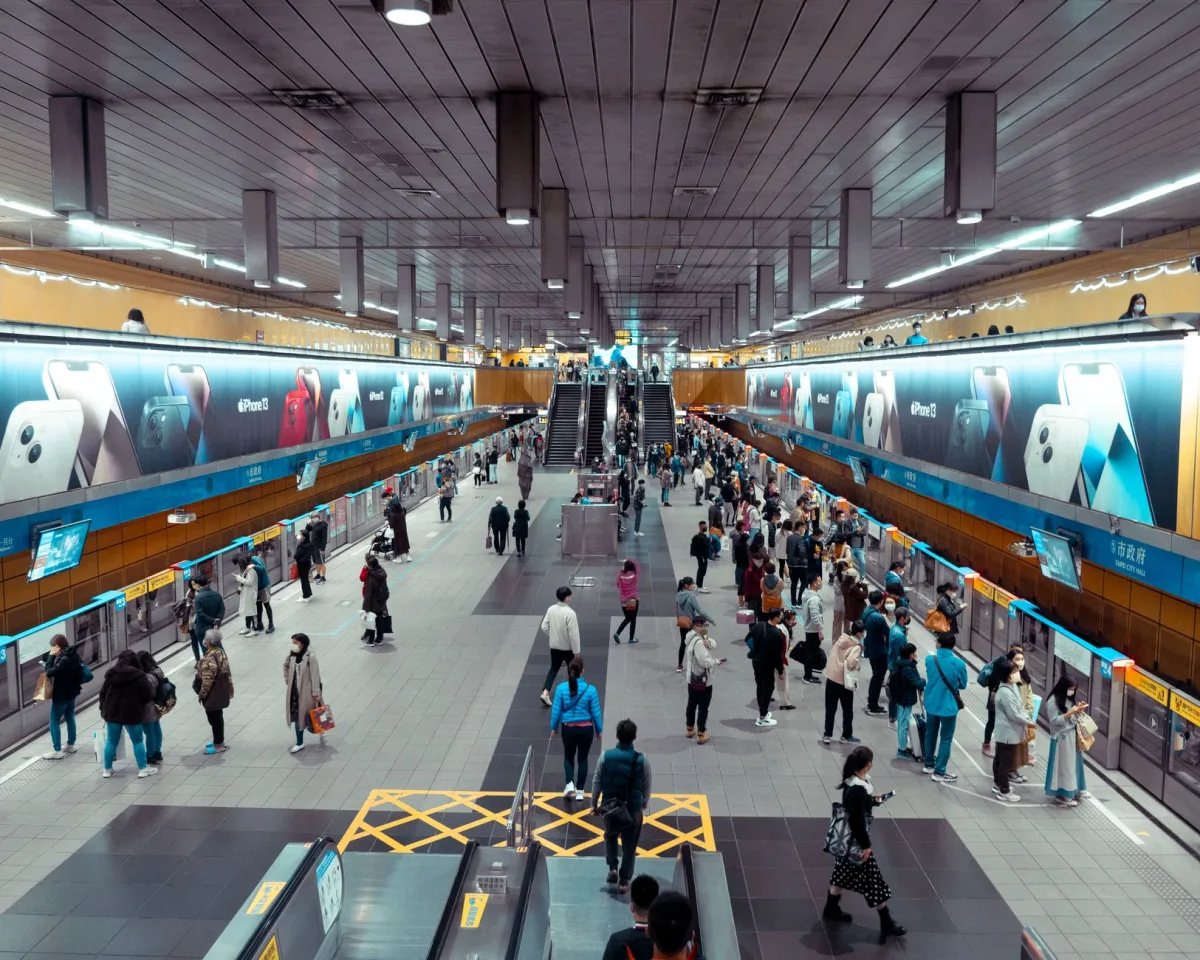 A bustling underground train station with people waiting and walking near escalators.
