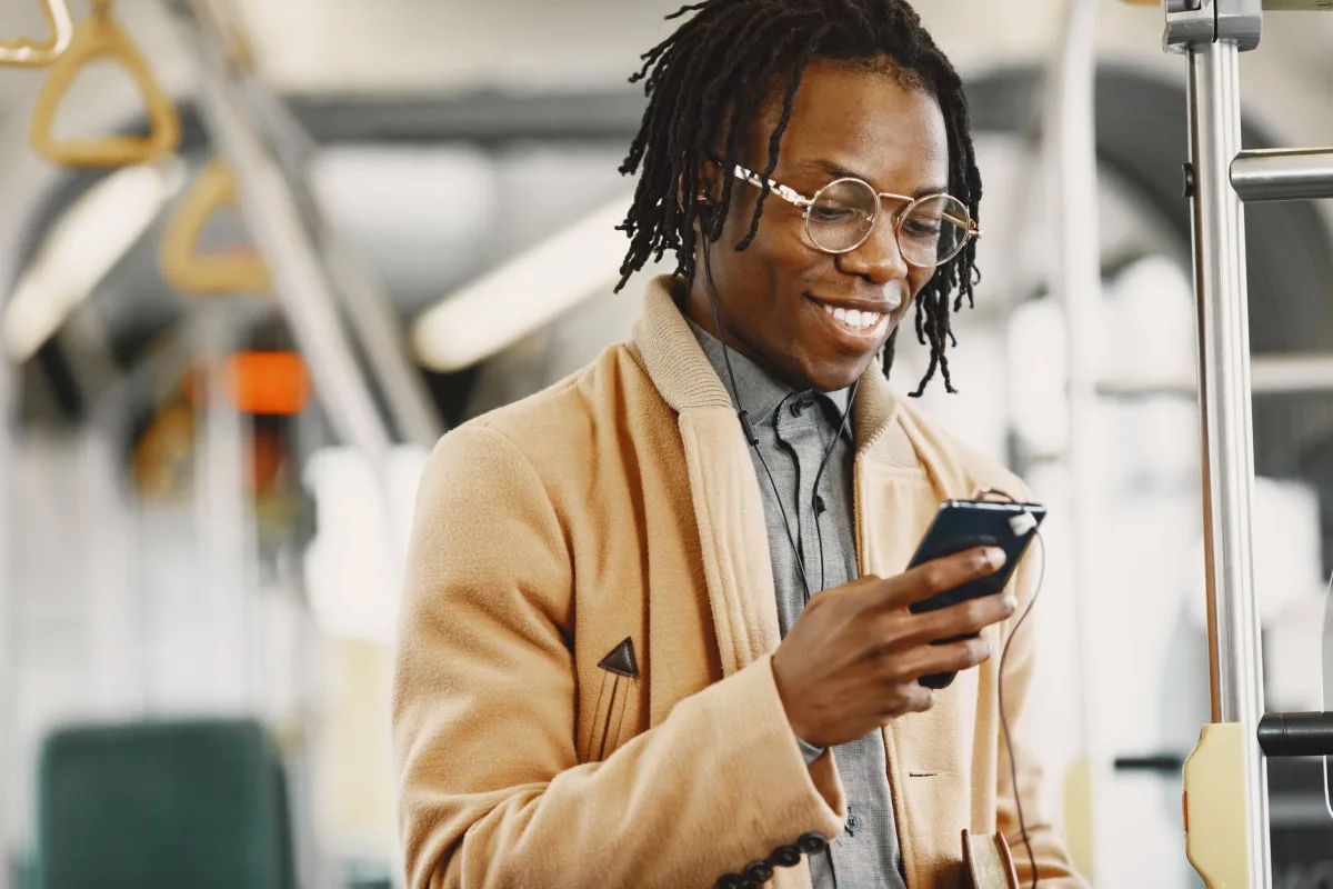 Stylish young man with dreadlocks smiling while using his phone during a commute on public transport.