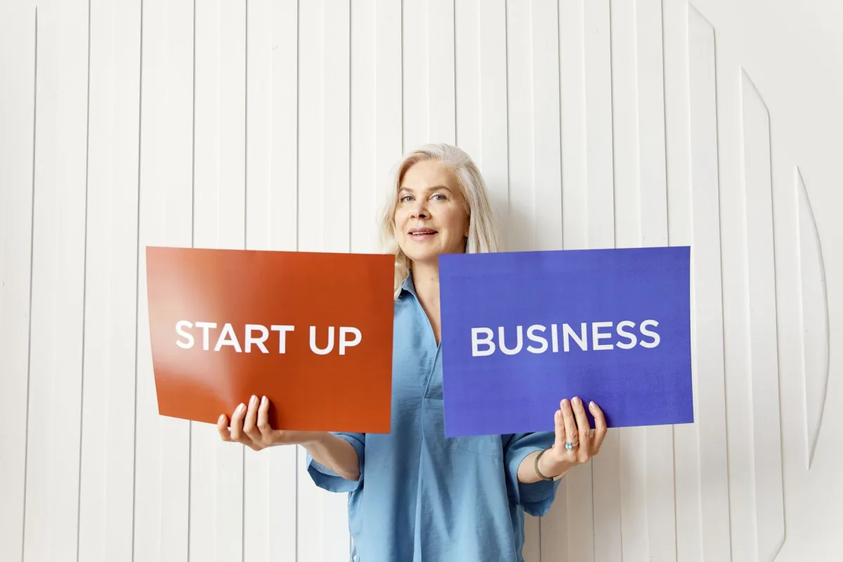 Elderly woman holding startup and business signs indoors against white background. Elderly woman holding startup and business signs indoors against white background.