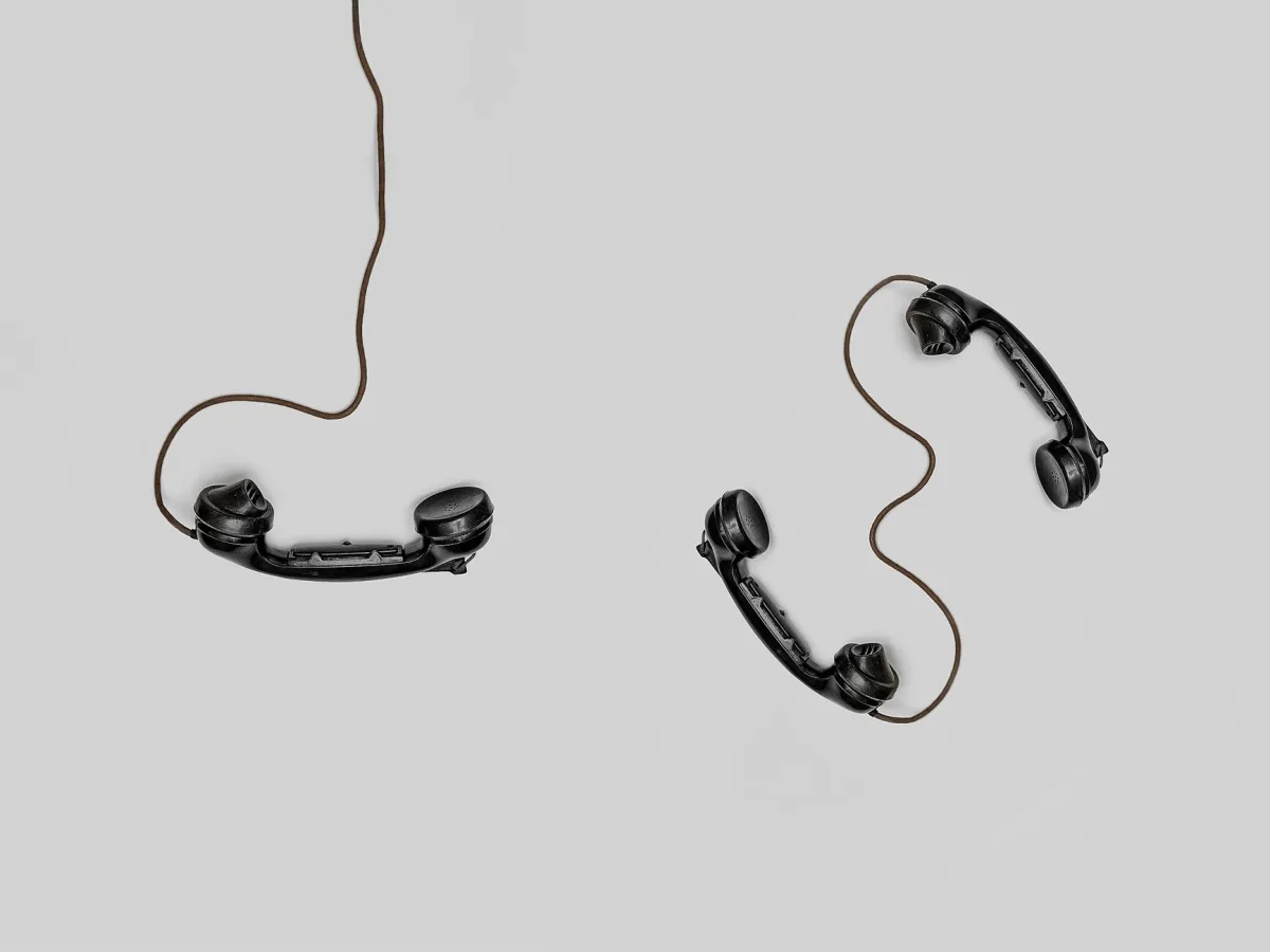 Two vintage black telephone handsets connected by cords on gray background. Two vintage black telephone handsets connected by cords on gray background.