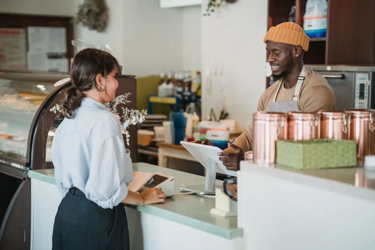 A barista and customer enjoy a friendly interaction at a café counter with a warm ambiance. A barista and customer enjoy a friendly interaction at a café counter with a warm ambiance.