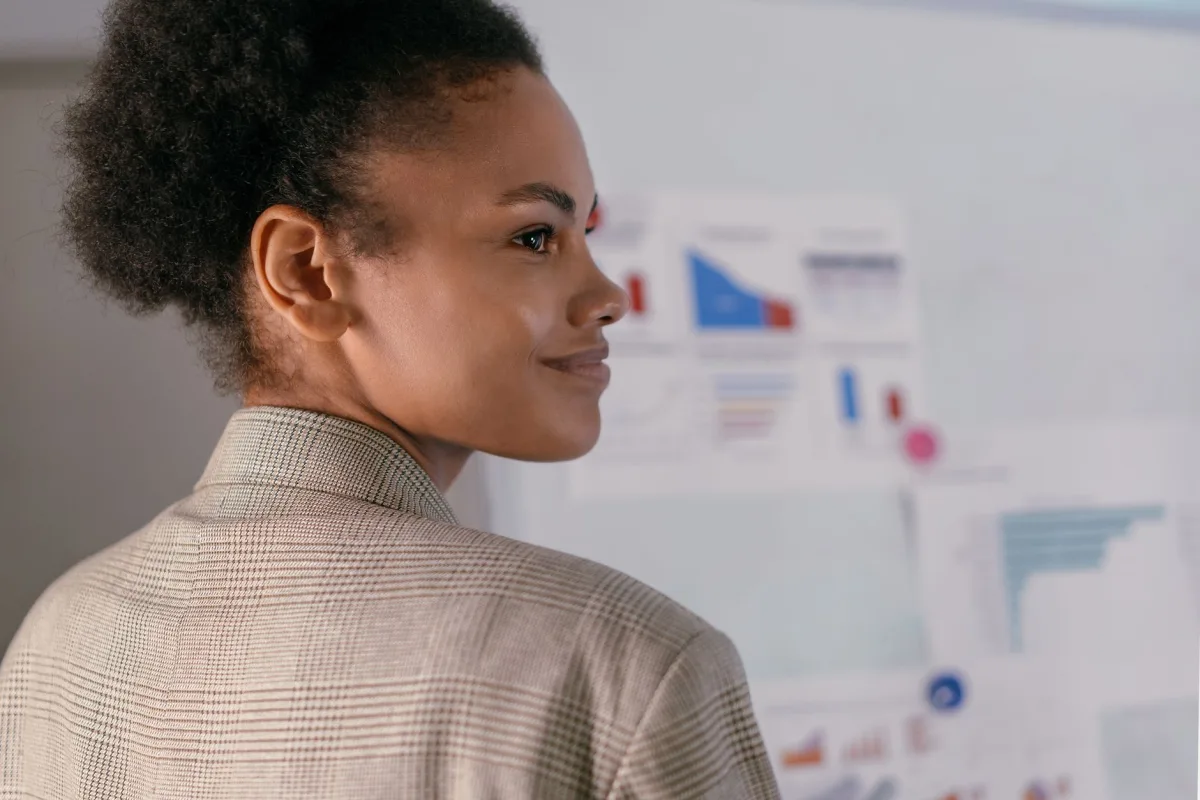 A confident businesswoman with curly hair smiling while presenting data charts in an office.