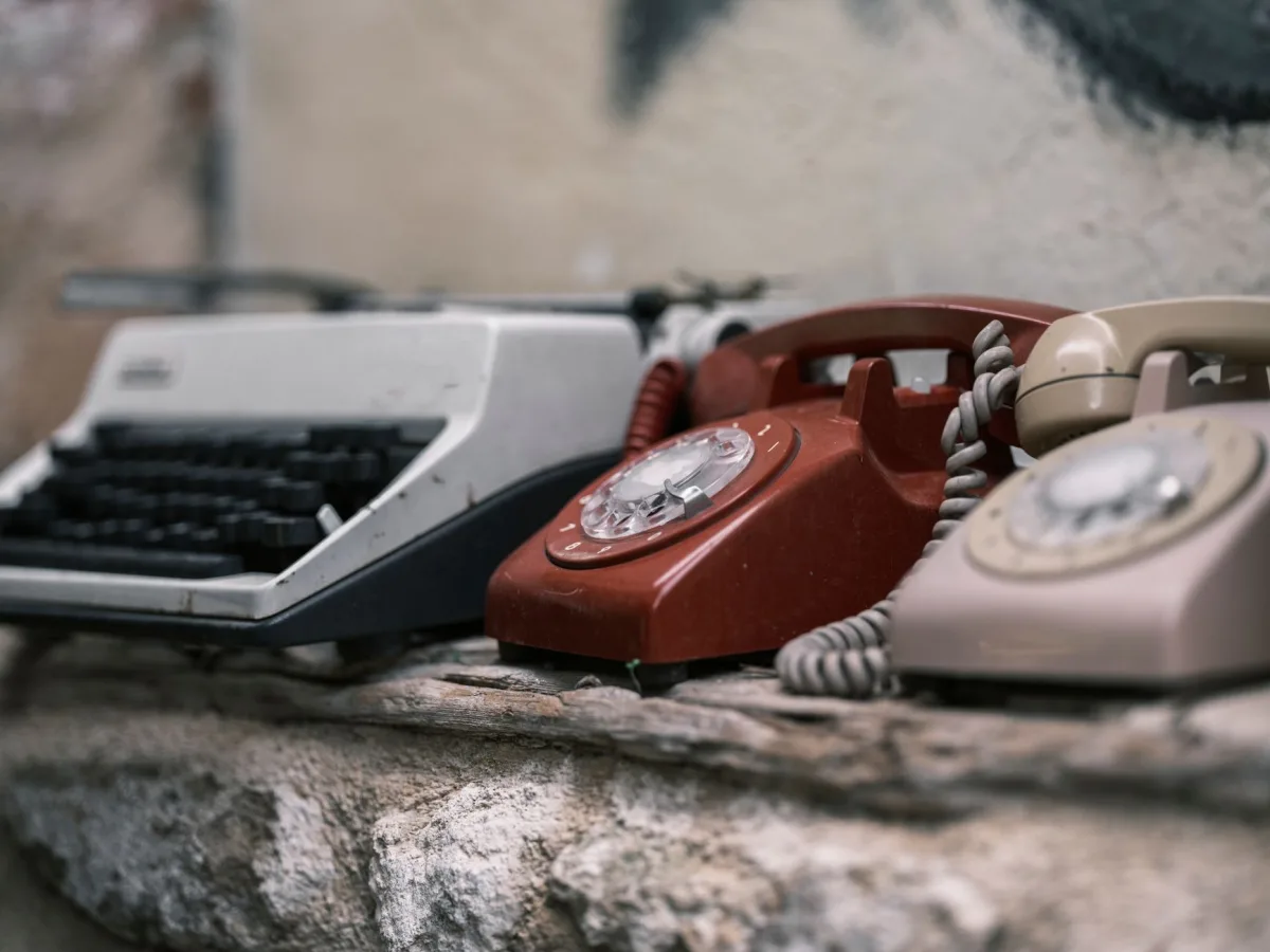 Rustic display of an old typewriter and rotary phones, embodying nostalgia. Rustic display of an old typewriter and rotary phones, embodying nostalgia.