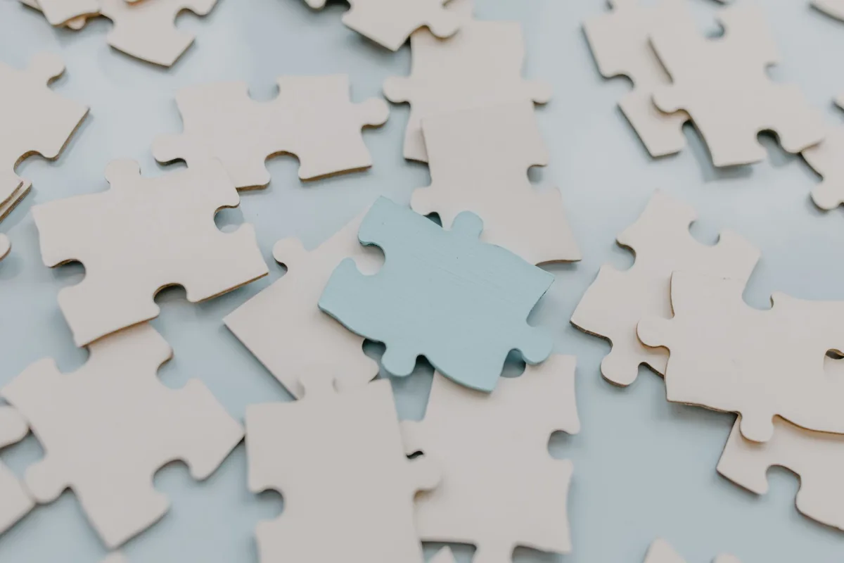 A close-up view of scattered puzzle pieces on a light background, featuring a unique blue piece.