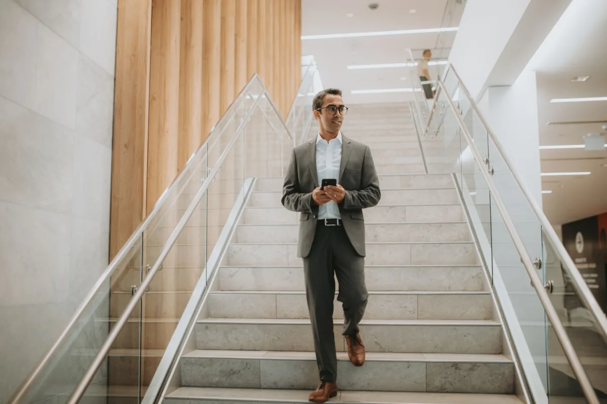 Confident businessman in suit walking downstairs while using a smartphone.