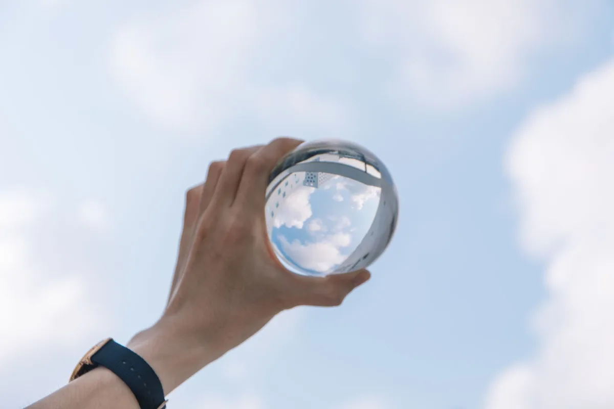 Unrecognizable male holding glass sphere inverse illustration in hand in sunny day under sky with clouds