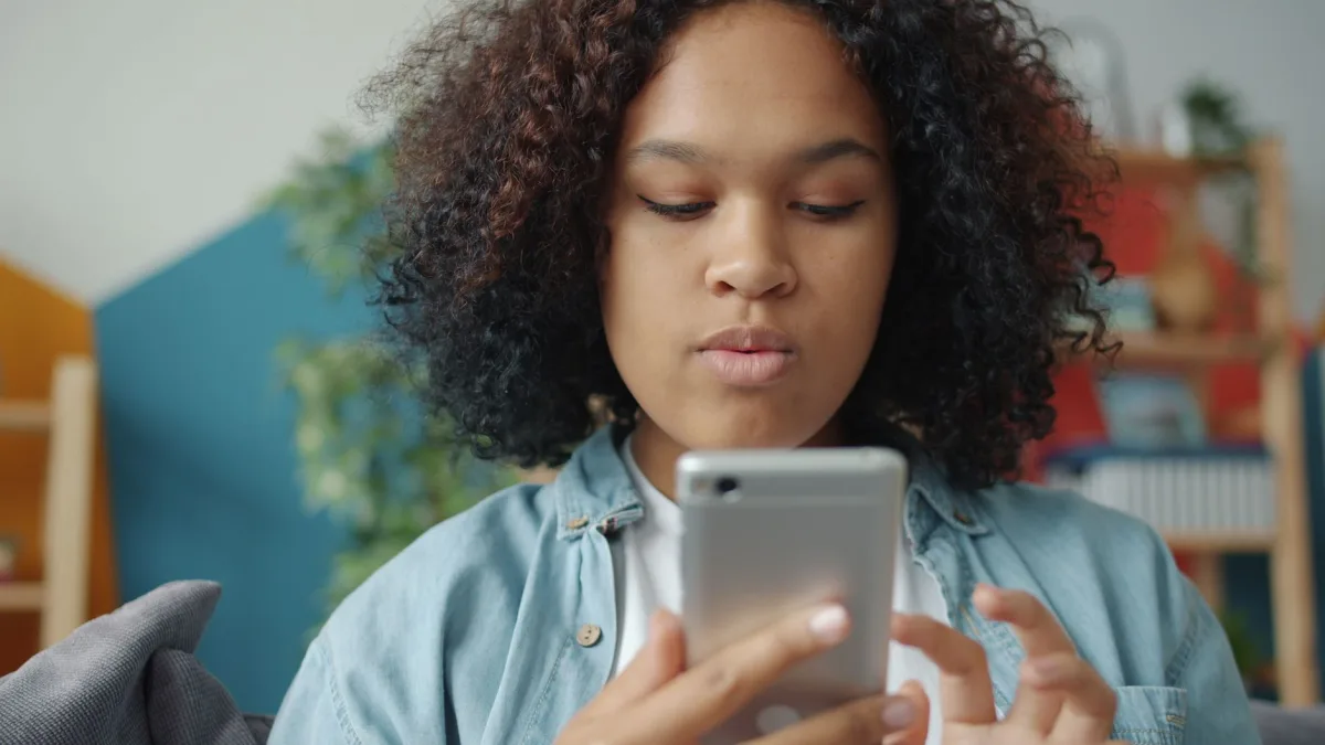 Teenage girl focused on her smartphone at home, with a cozy indoor background.
