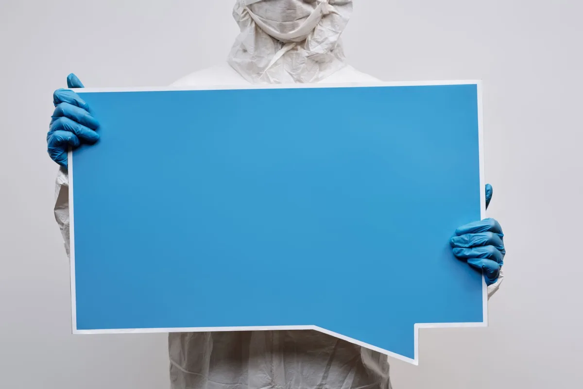 A person wearing protective gear holding a large blue speech bubble placard with copy space. A person wearing protective gear holding a large blue speech bubble placard with copy space.