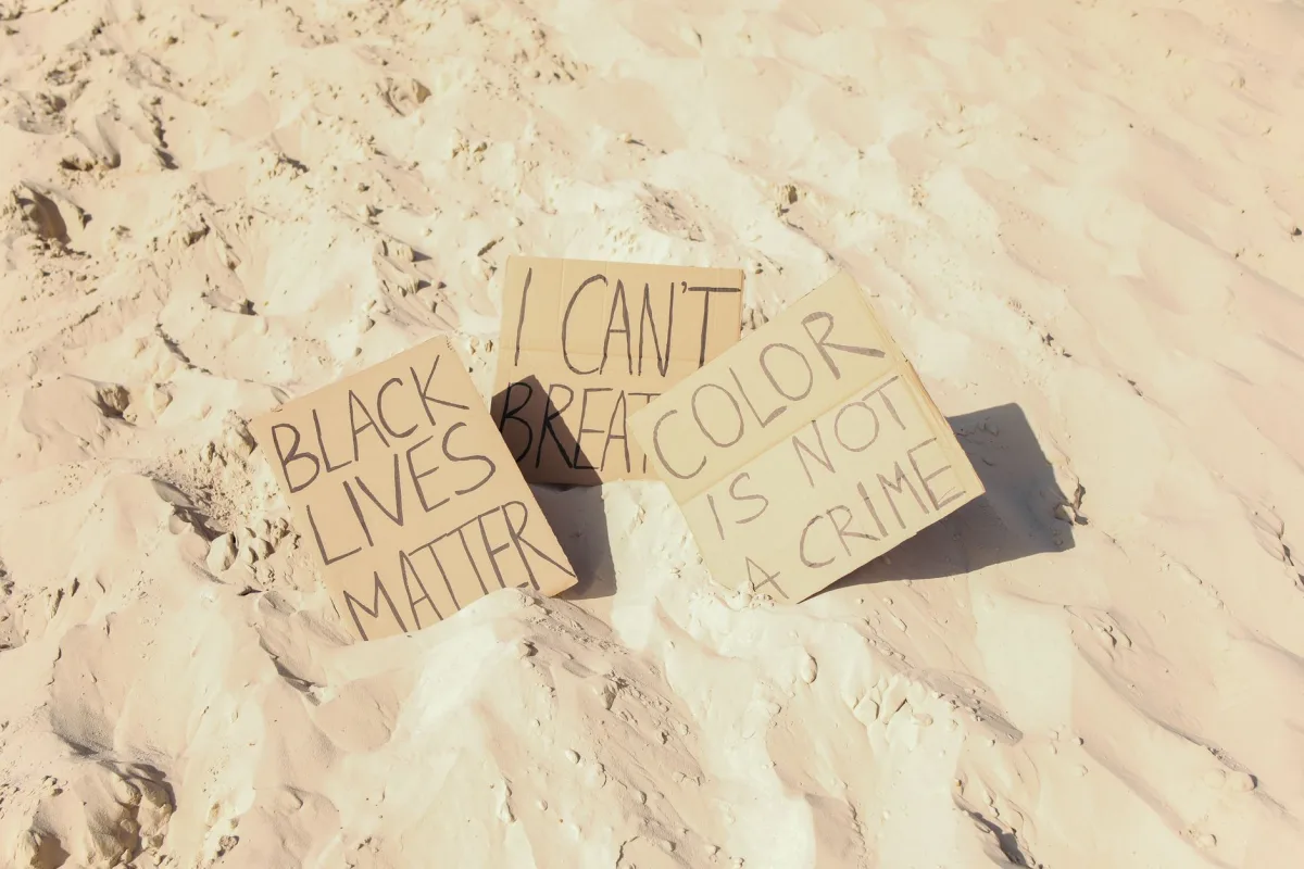 Cardboard protest signs on sand with messages against racism and for equality.