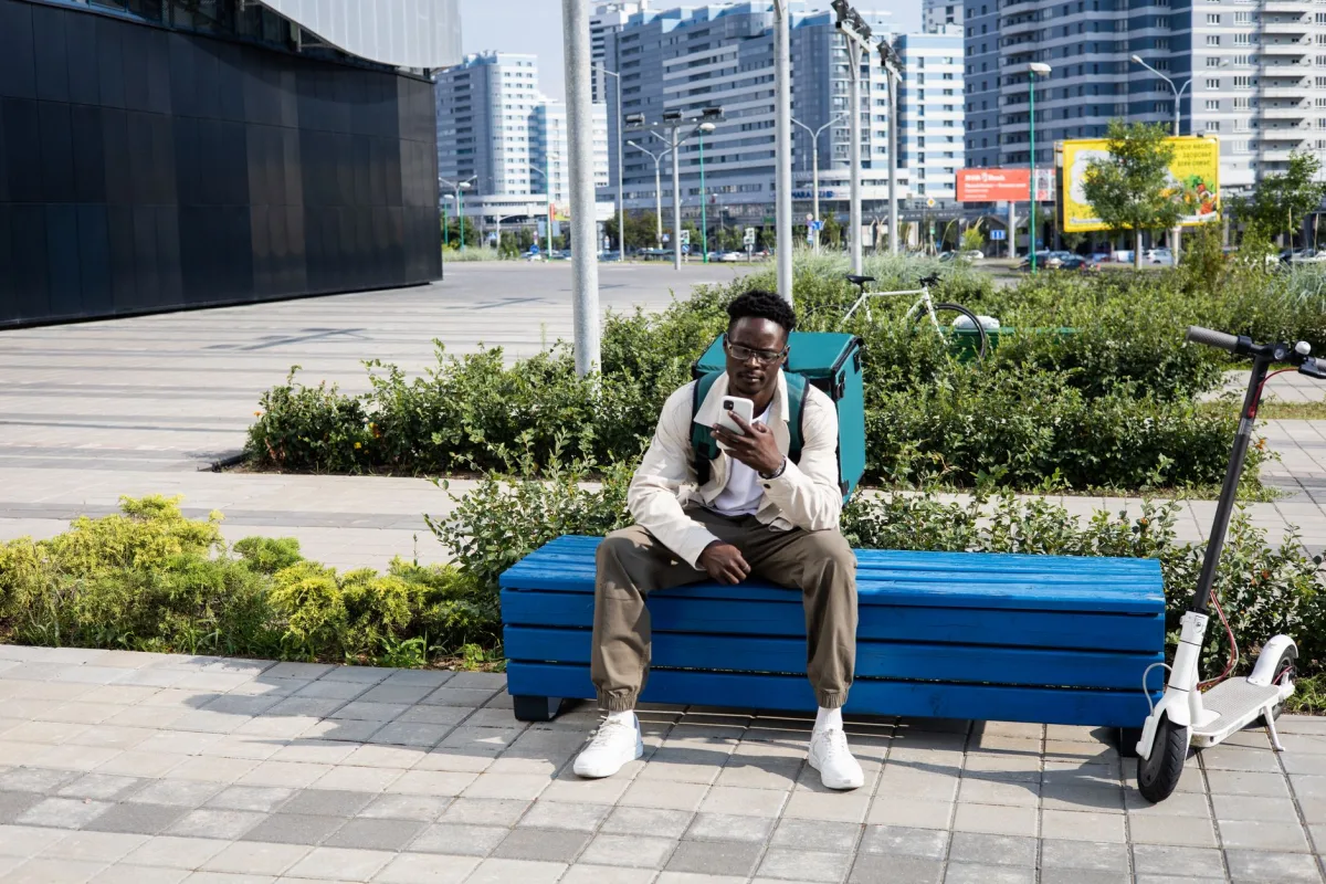 Young man on a break with electric scooter and thermal bag in modern cityscape.