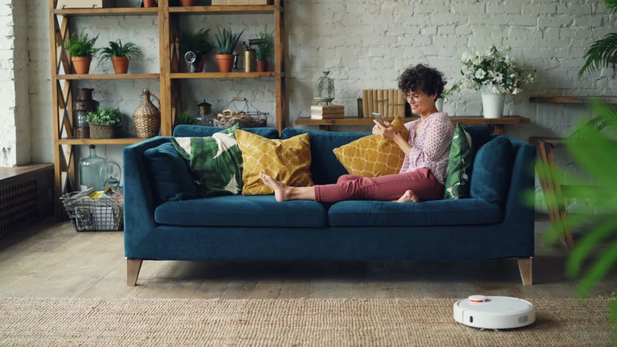 Adult enjoying a relaxing day on a cozy sofa with a phone and cleaning robot. Adult enjoying a relaxing day on a cozy sofa with a phone and cleaning robot.