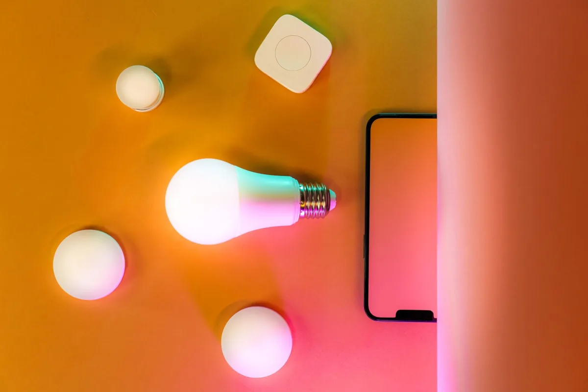 Modern home lighting setup featuring a glowing LED bulb and gadget on an orange background. Modern home lighting setup featuring a glowing LED bulb and gadget on an orange background.