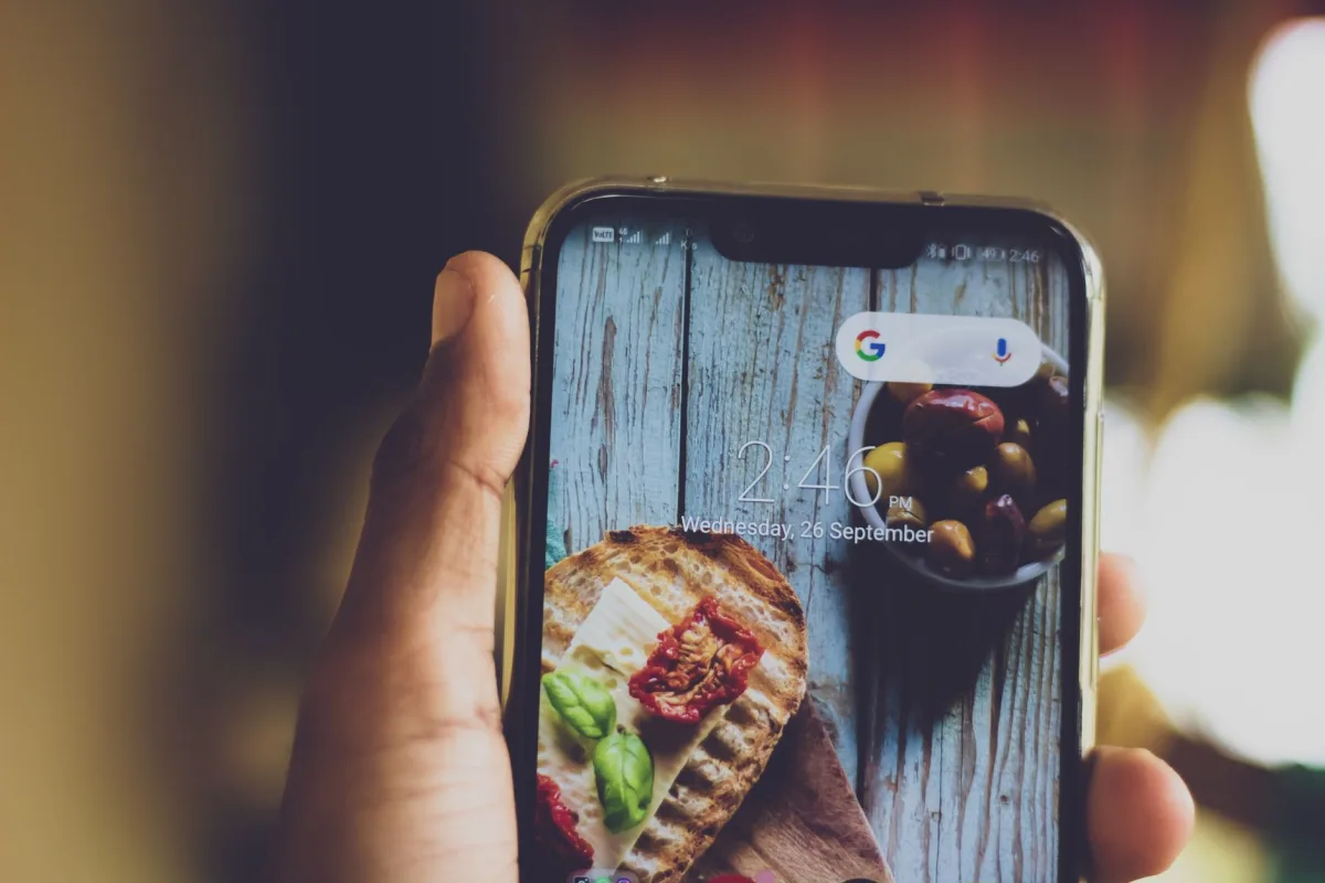 Close-up of a hand holding a smartphone displaying a food image on its screen, indoors. Close-up of a hand holding a smartphone displaying a food image on its screen, indoors.
