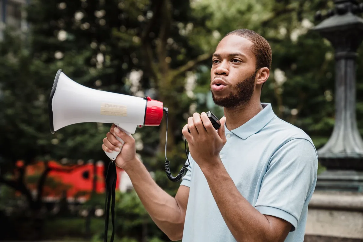 A passionate activist uses a megaphone to promote nonviolence during a protest outdoors. A passionate activist uses a megaphone to promote nonviolence during a protest outdoors.