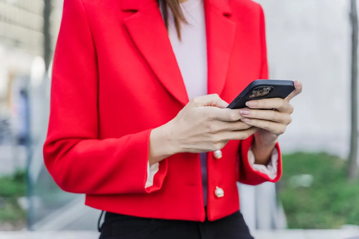 Close-up a woman in a vibrant red blazer using a smartphone outdoors during daytime.