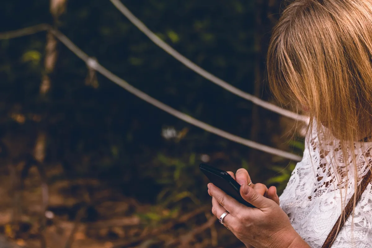 Woman focusing on mobile phone while outdoors in a natural setting.