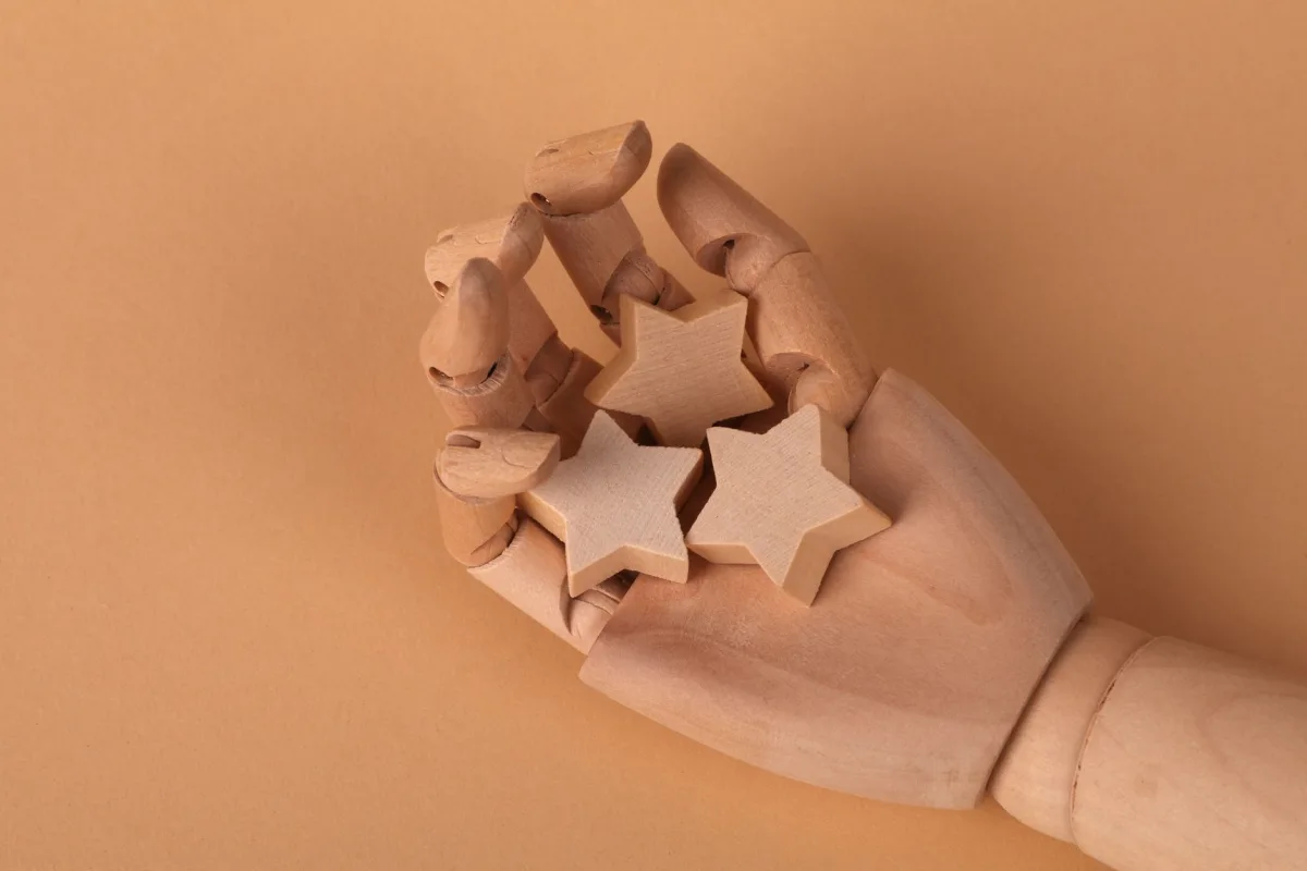 A wooden mannequin hand holding three wooden stars against a beige background, symbolizing creativity and craftsmanship. A wooden mannequin hand holding three wooden stars against a beige background, symbolizing creativity and craftsmanship.