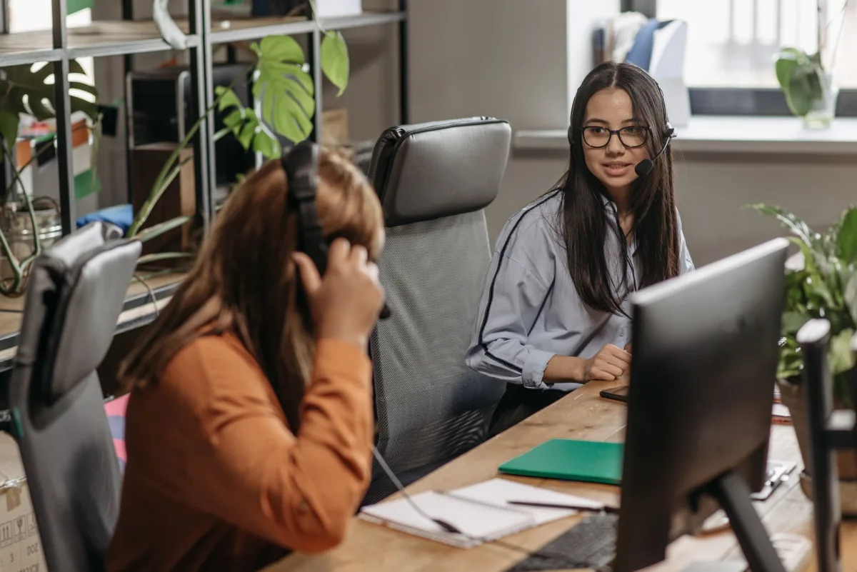 Two women working together a vibrant office space, wearing headsets and engaging teamwork.