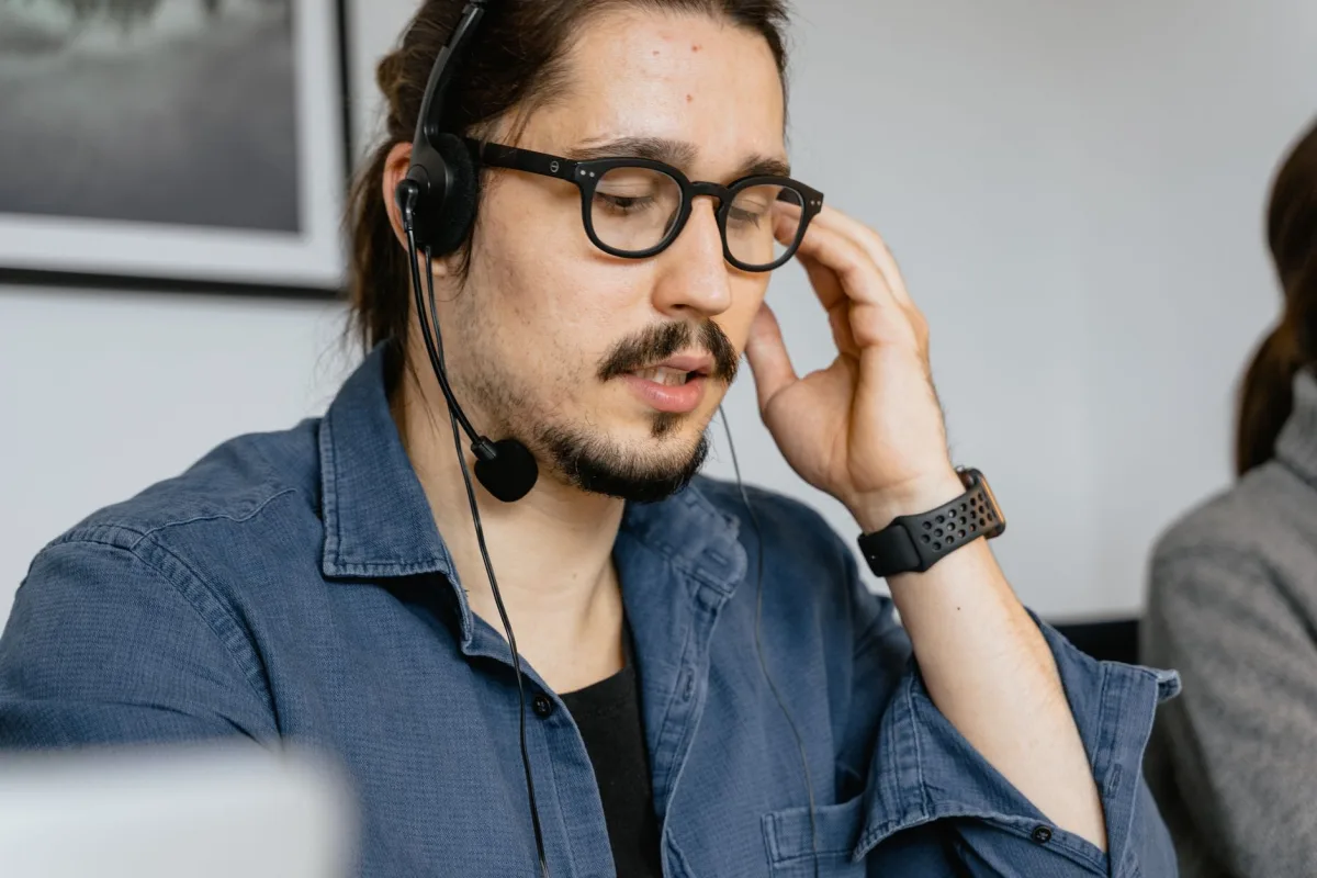 A bearded man with glasses and headphones working a call center, providing customer
