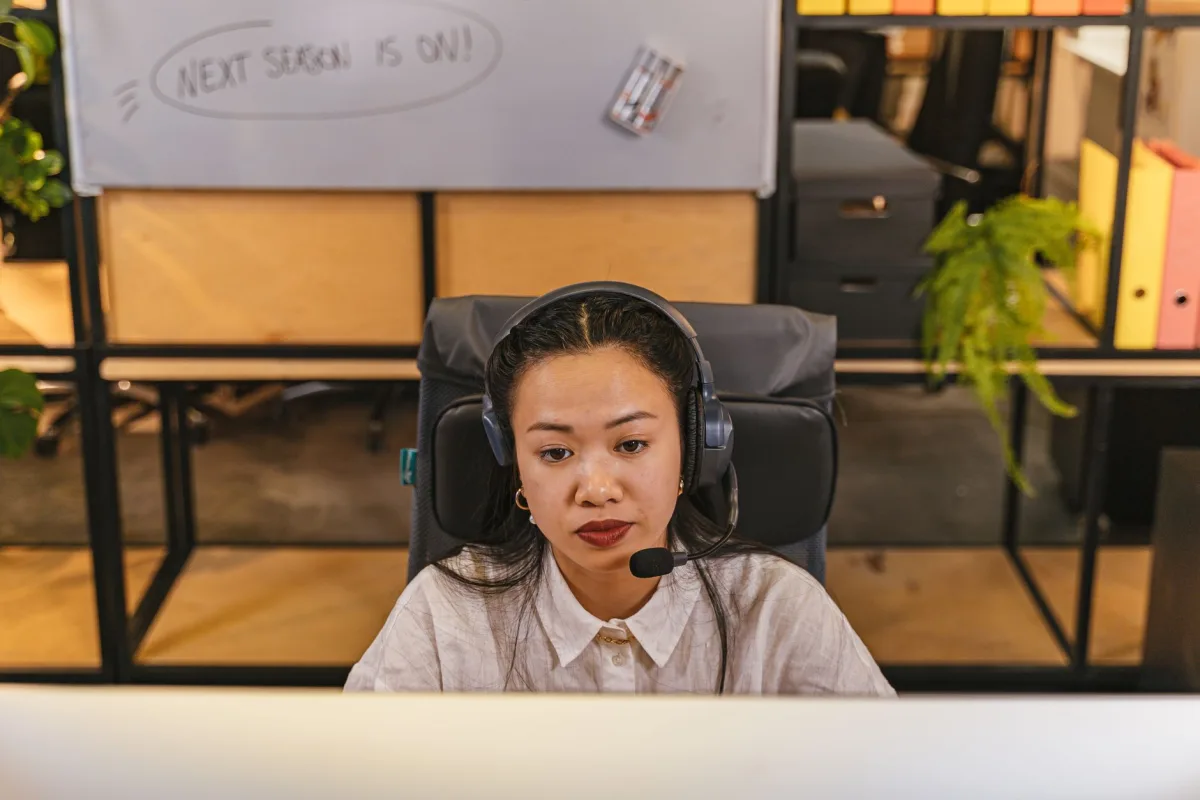 Young woman focused on work, using headset in modern office environment.