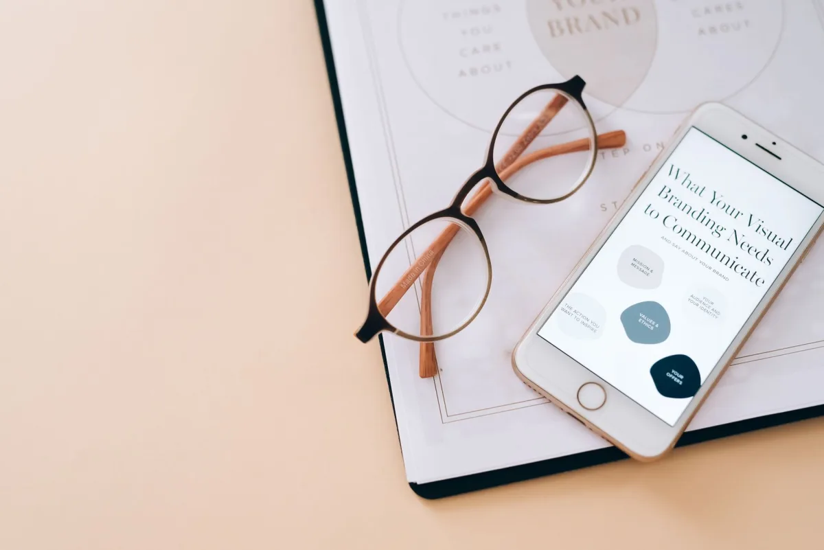 Stylish flat lay of eyeglasses, smartphone, and branding document on a desk. Stylish flat lay of eyeglasses, smartphone, and branding document on a desk.