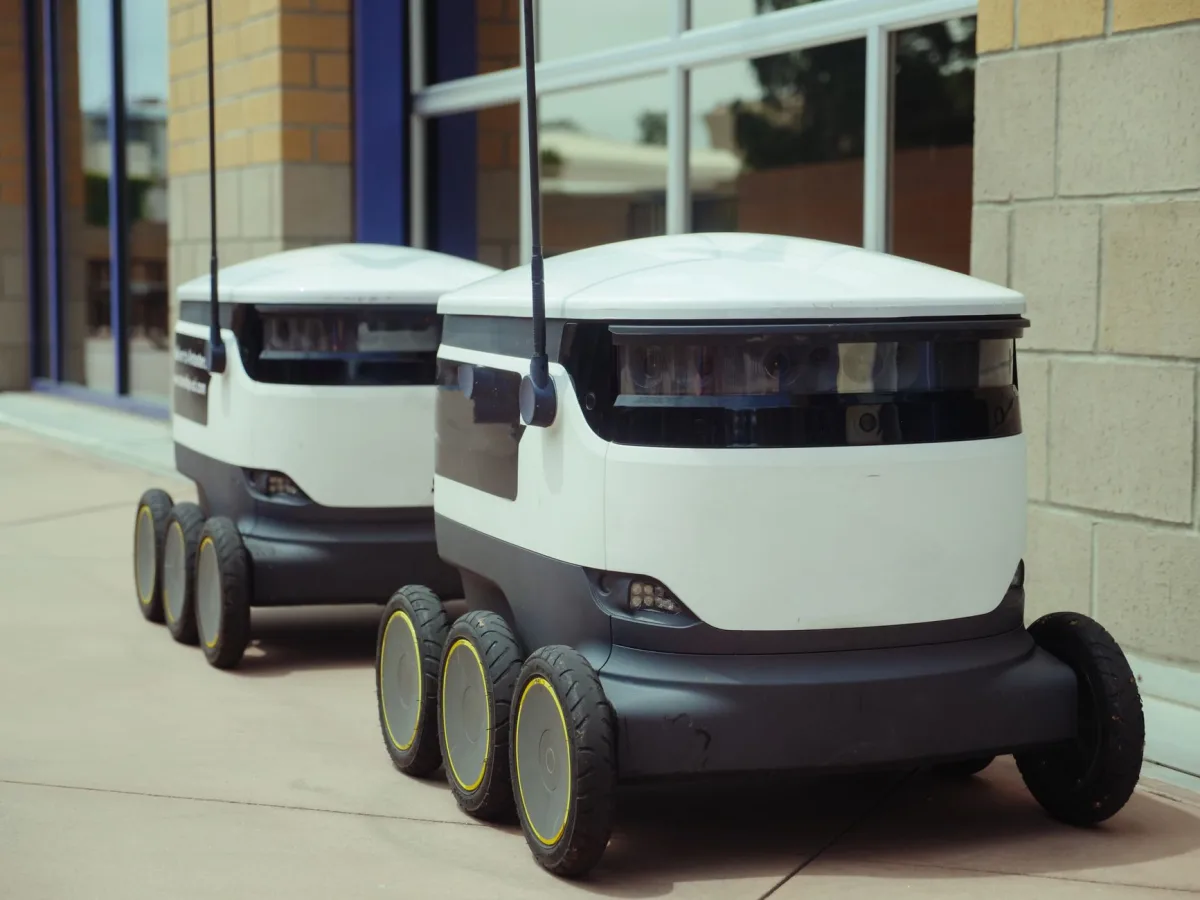Two delivery robots positioned outside a modern building, showcasing innovation in robotics and mobility. Two delivery robots positioned outside a modern building, showcasing innovation in robotics and mobility.