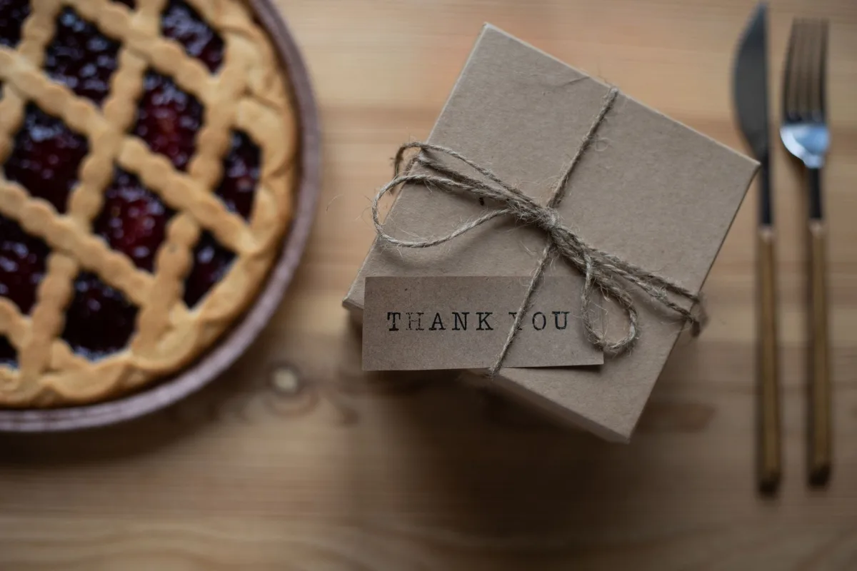 Top view of carton gift box tied with rope and decorated with small postcard with inscription on table with sweet pie and knife with fork Top view of carton gift box tied with rope and decorated with small postcard with inscription on table with sweet pie and knife with fork