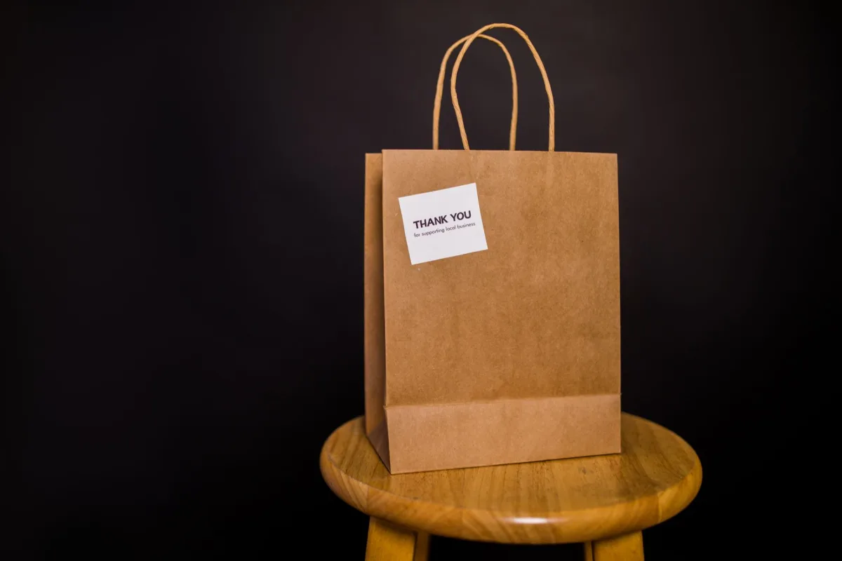 Brown paper bag with note placed on a wooden stool against a black background. Brown paper bag with note placed on a wooden stool against a black background.