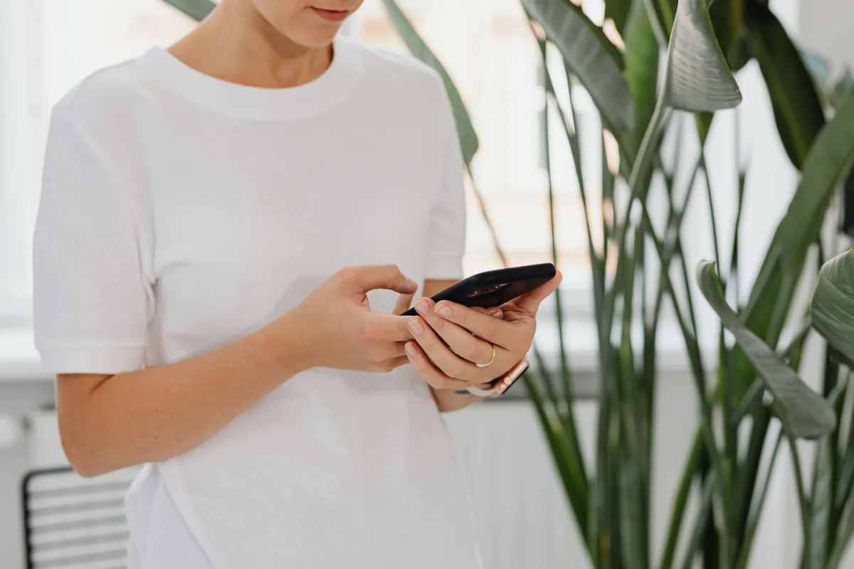 A woman uses a smartphone indoors surrounded by lush green plants. A woman uses a smartphone indoors surrounded by lush green plants.