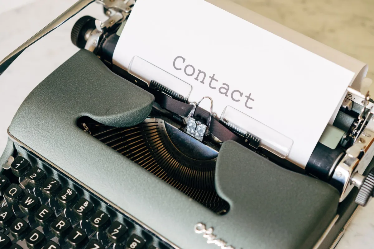 Close-up of a vintage typewriter typing the word 'Contact' on paper, evoking nostalgia.