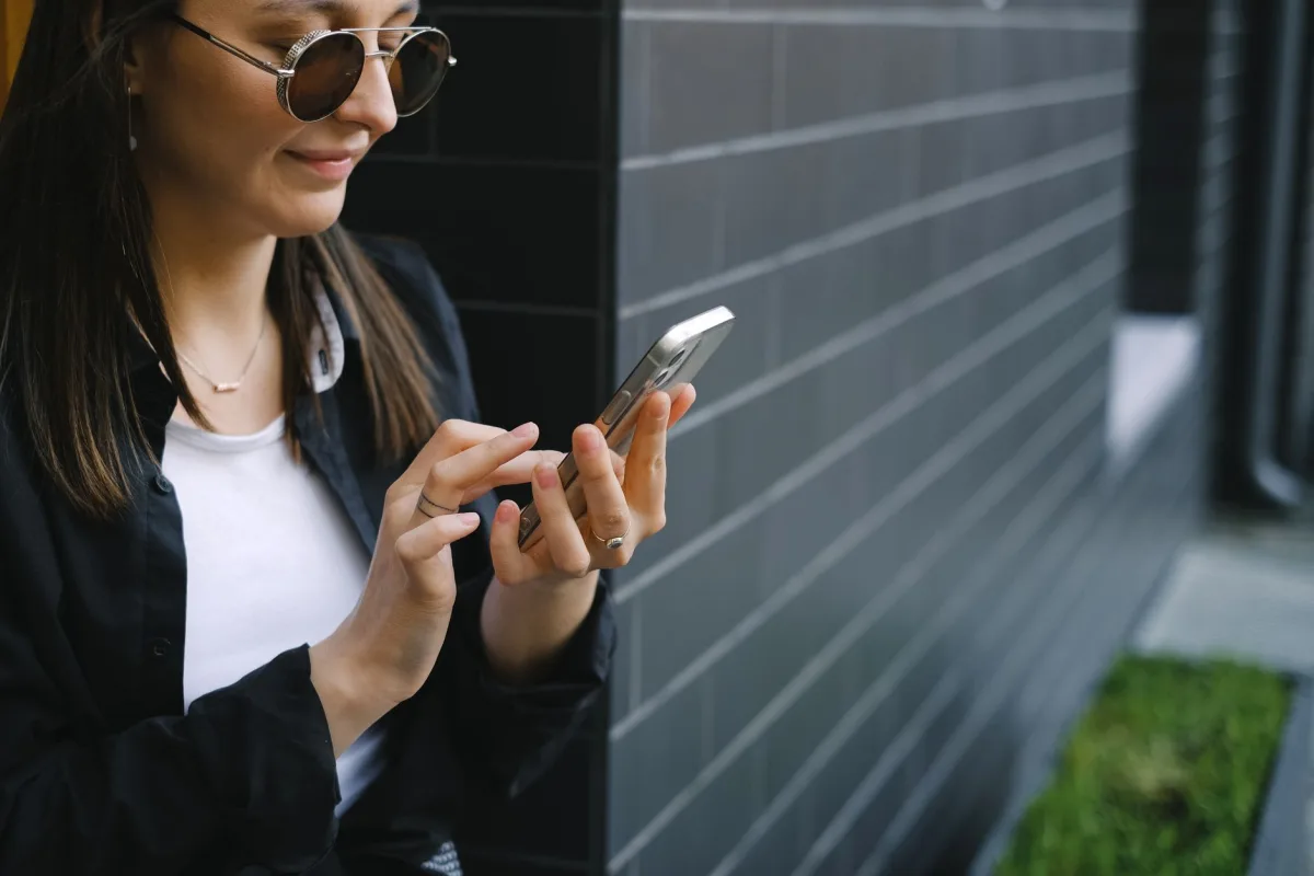 Confident young woman using smartphone outdoors by a modern building facade. Confident young woman using smartphone outdoors by a modern building facade.