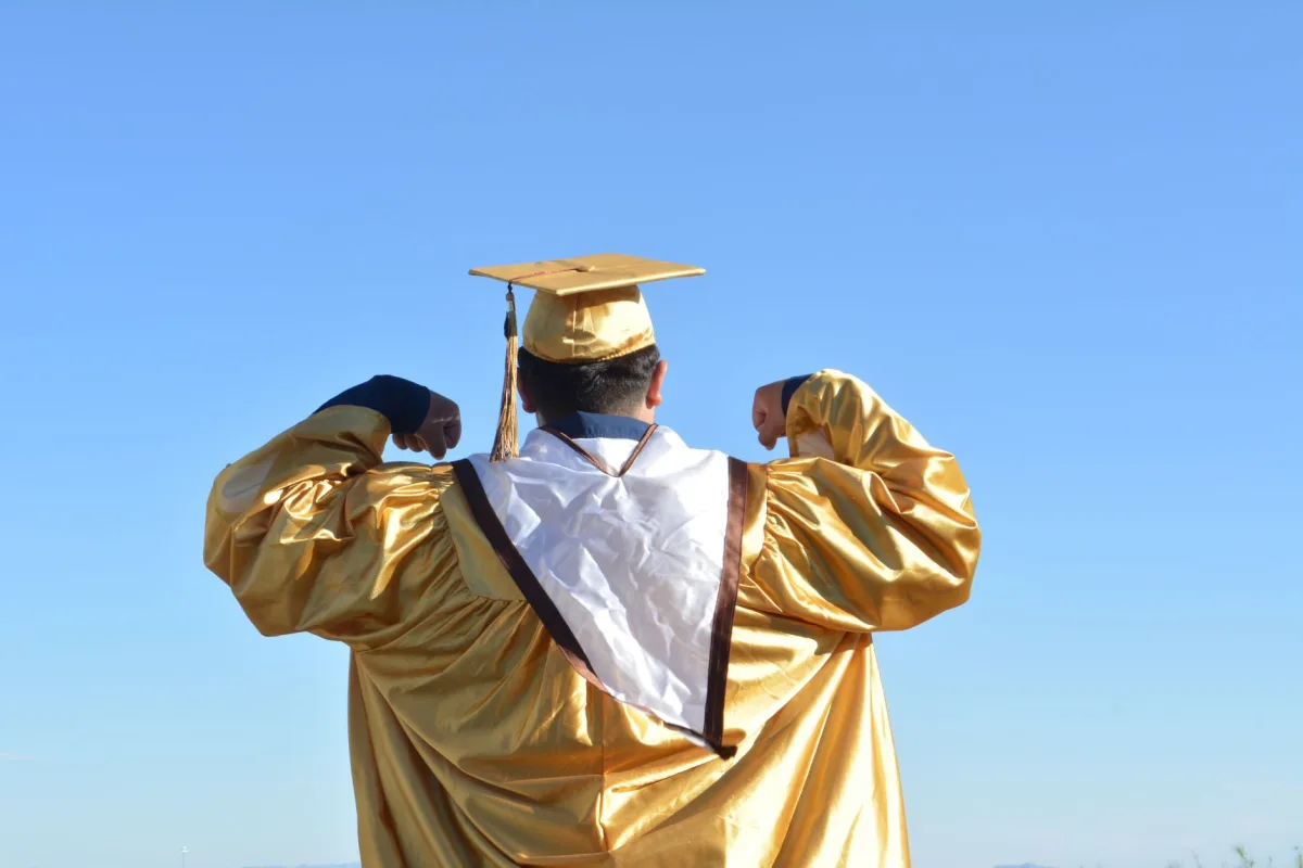 Graduate in gold gown celebrates achievement beneath clear blue skies. Graduate in gold gown celebrates achievement beneath clear blue skies.