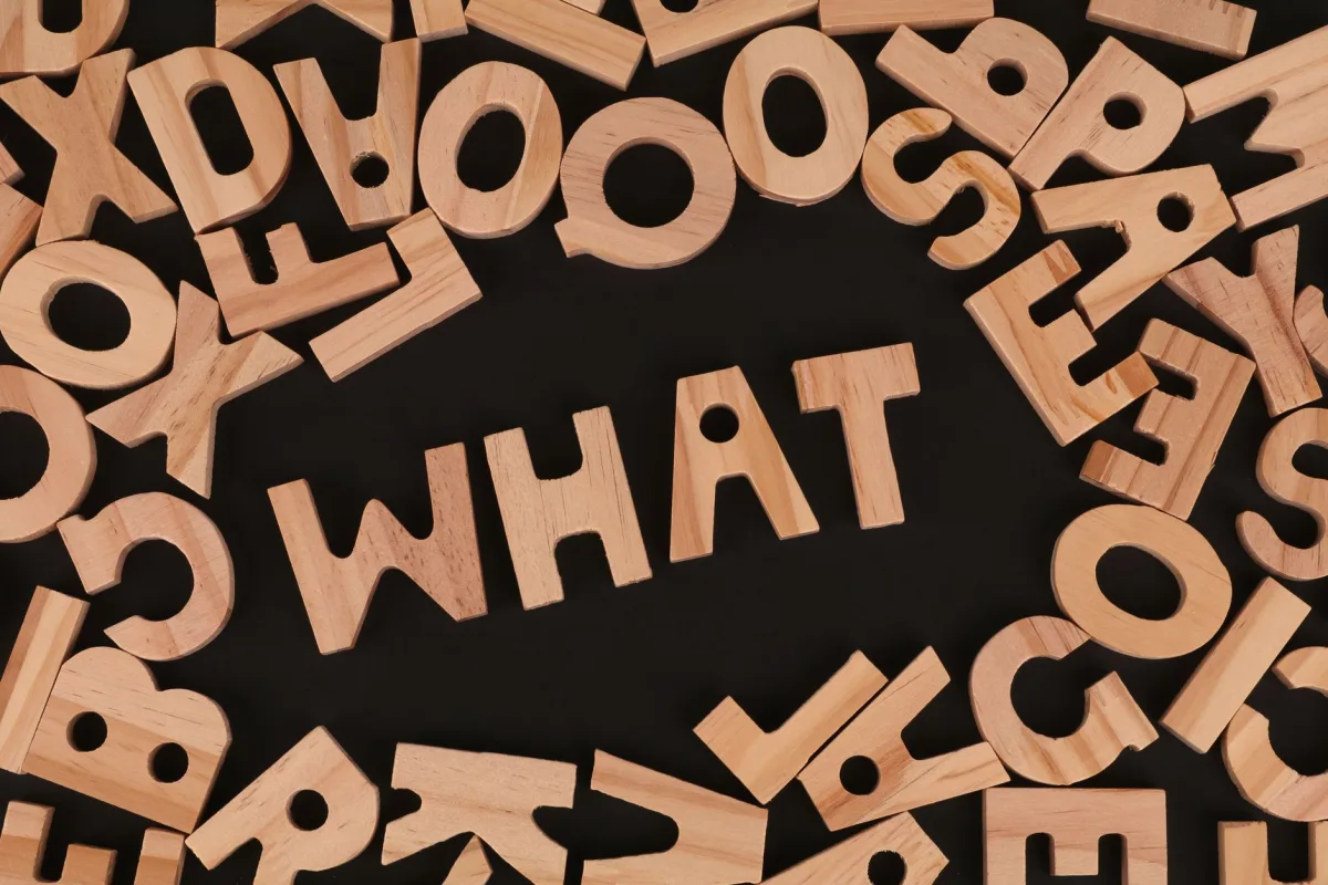 Artistic arrangement of wooden letters spelling 'WHAT' on a black background, offering creative inspiration.