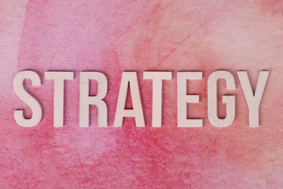 Wooden letters spelling 'Strategy' on a pink textured background. Wooden letters spelling 'Strategy' on a pink textured background.