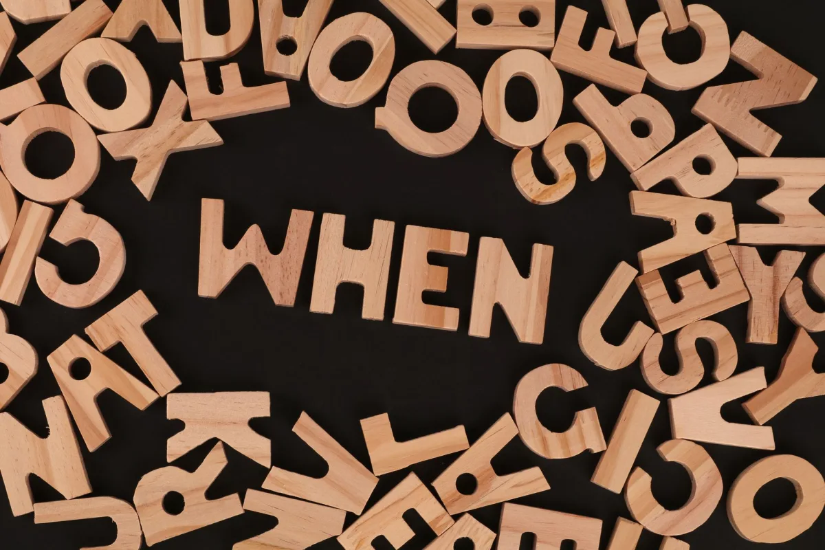 Scattered wooden alphabet letters with the word 'WHEN' on a black surface, creative concept.