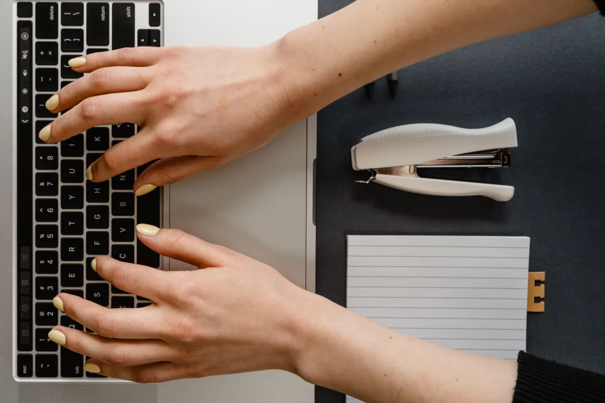 Top view of hands typing on keyboard with stationary items around. Top view of hands typing on keyboard with stationary items around.