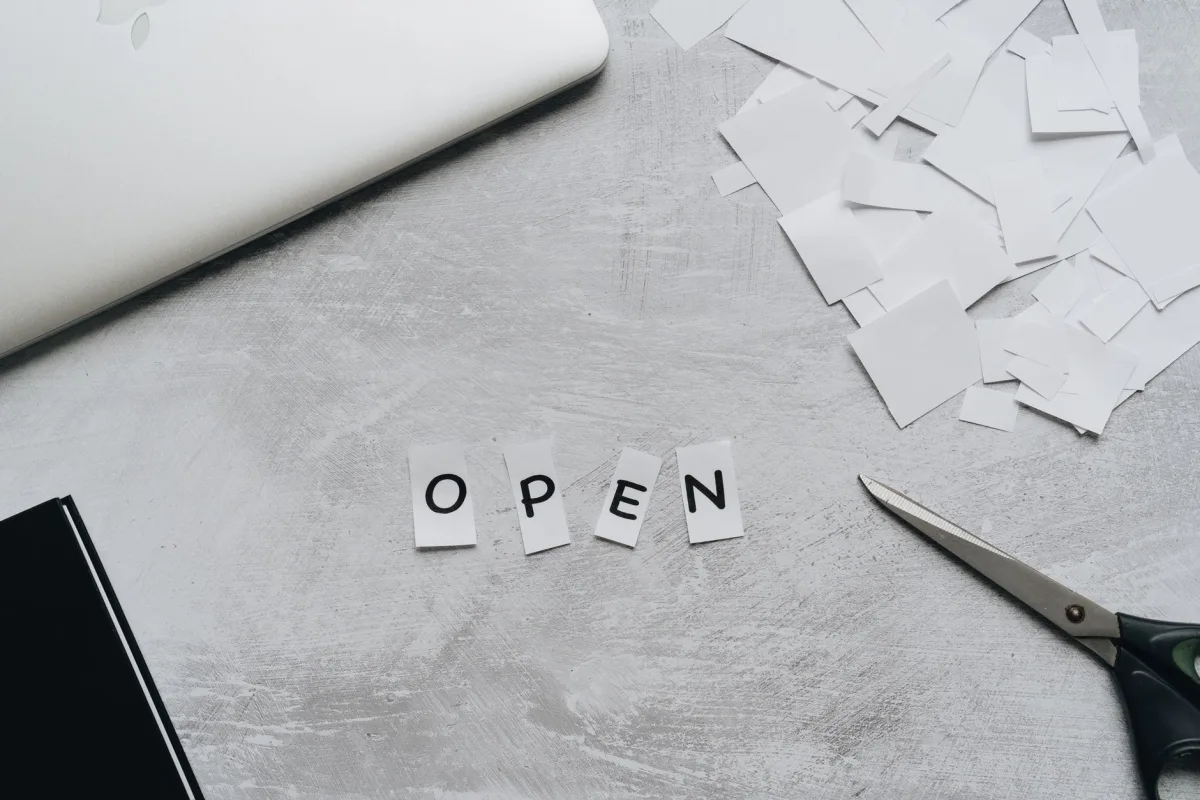Flat lay of a creative workspace with paper letters spelling 'OPEN,' scissors, and a laptop. Flat lay of a creative workspace with paper letters spelling 'OPEN,' scissors, and a laptop.