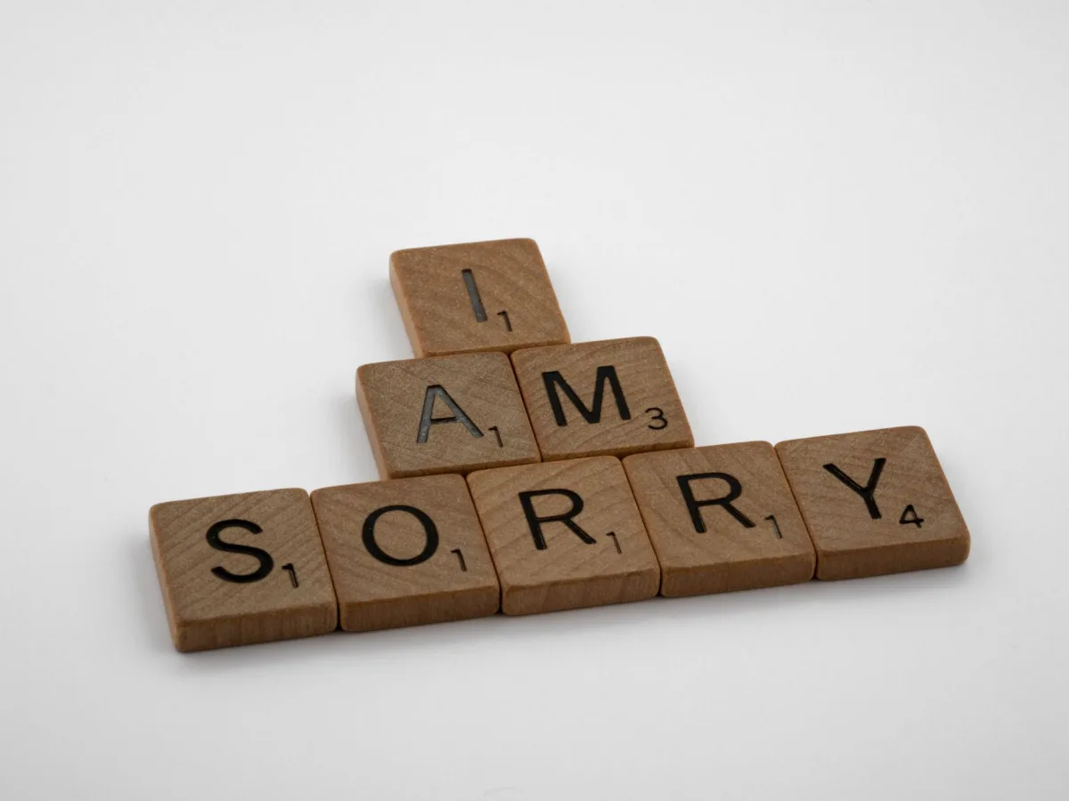 Wooden Scrabble tiles arranged to say 'I Am Sorry' on a clean white background, conveying a message of